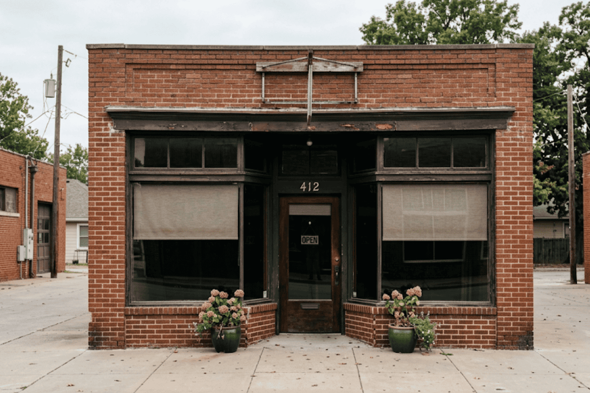 Brick storefront with large front windows, door marked 412, and an open sign; two potted plants flank the entrance.